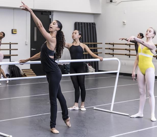 Graf Mack demonstrates a movement at the barre while students follow in a studio setting